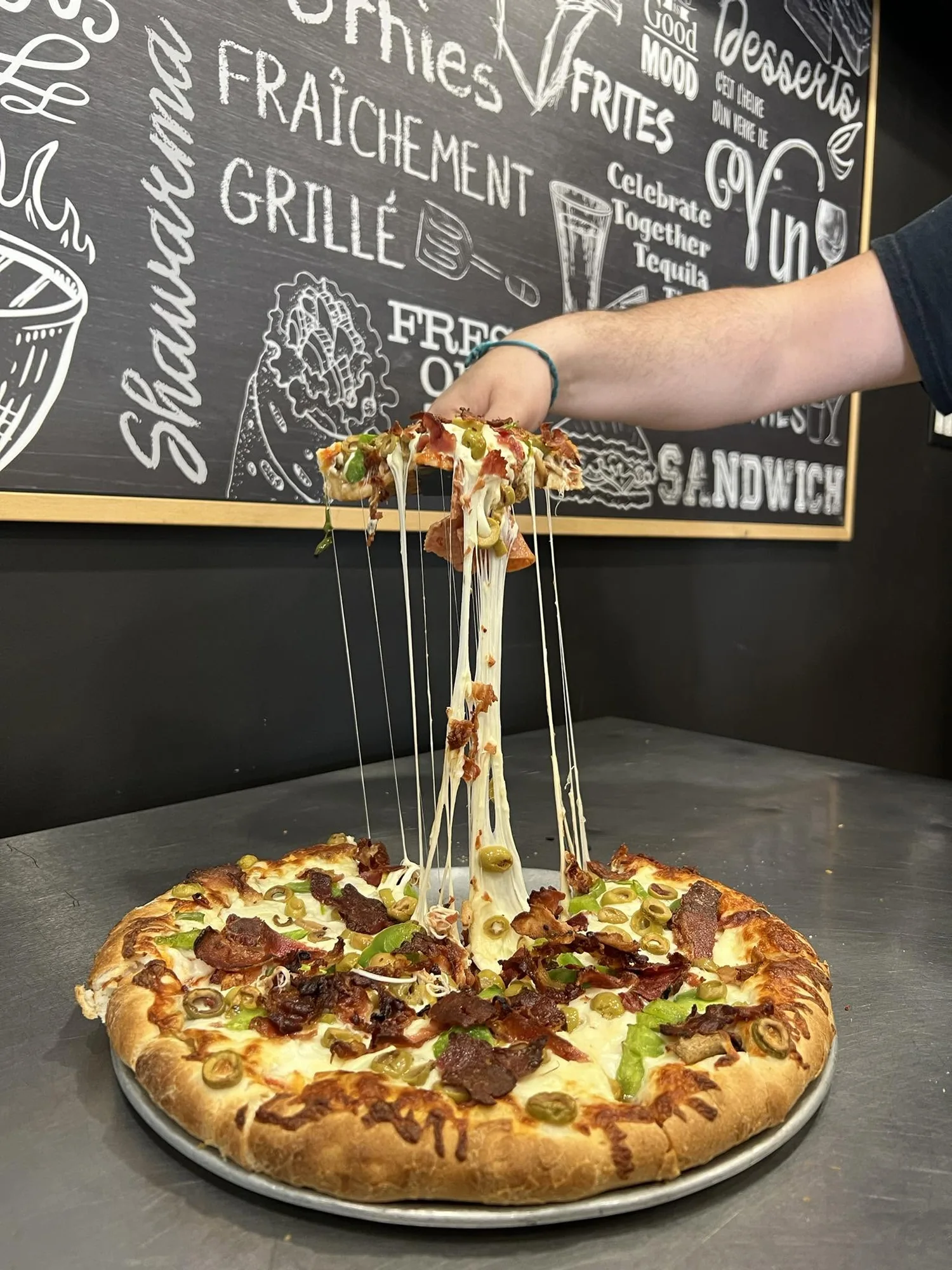 Une pizza bien garnie au fromage filant, devant le mur-tableau de Pizza Express